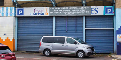 A silver car is parked in front of a blue and white building. Description generated by AI