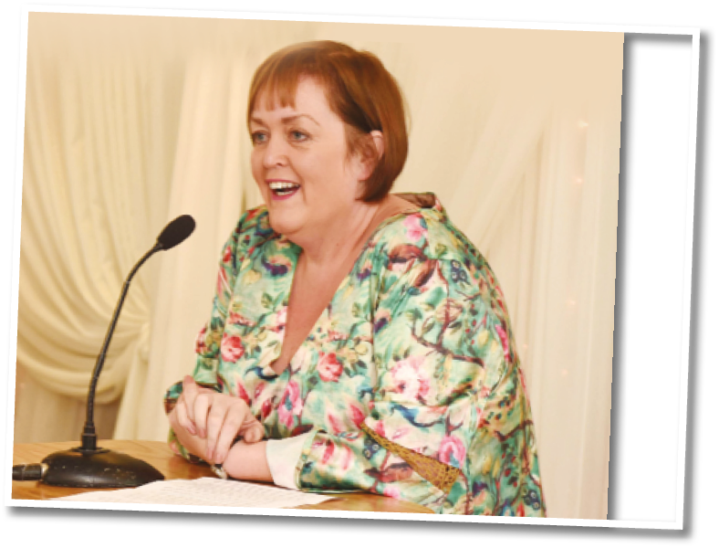 A woman wearing a floral print dress and standing at a podium. Description generated by AI