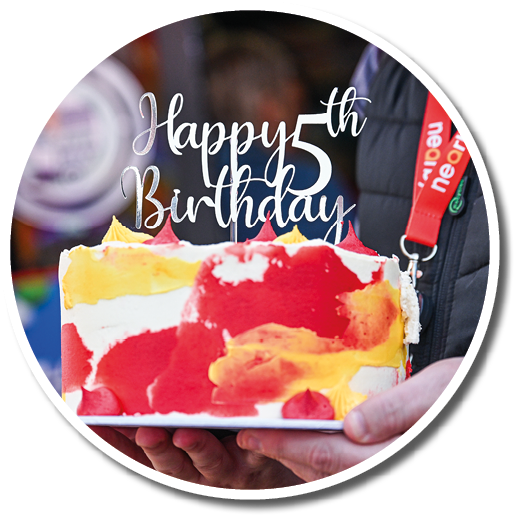 A person holding a cake with red, orange, and yellow frosting. Description generated by AI