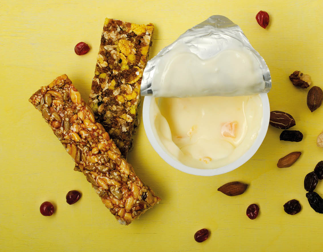 A bowl of yogurt with a spoon in it and two granola bars on the side. Description generated by AI