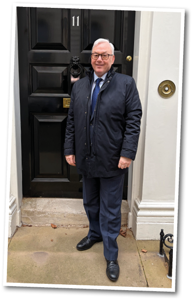 A man standing in front of a black door. Description generated by AI