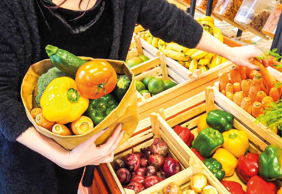 Woman in a supermarket at the vegetable shelf shopping for groceries, with bag of vegetables and fruits