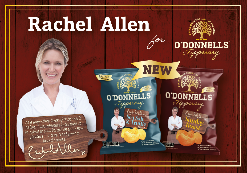 An adult with light hair wearing a white shirt stands next to two bags of O'Donnells crisps labeled Sea Salt & Truffle and Sunday Roast with a wooden cutting board featuring a handwritten note endorsing the brand. Description generated by AI