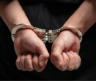 A person wearing black clothing has their hands cuffed behind their back with metal handcuffs. Description generated by AI