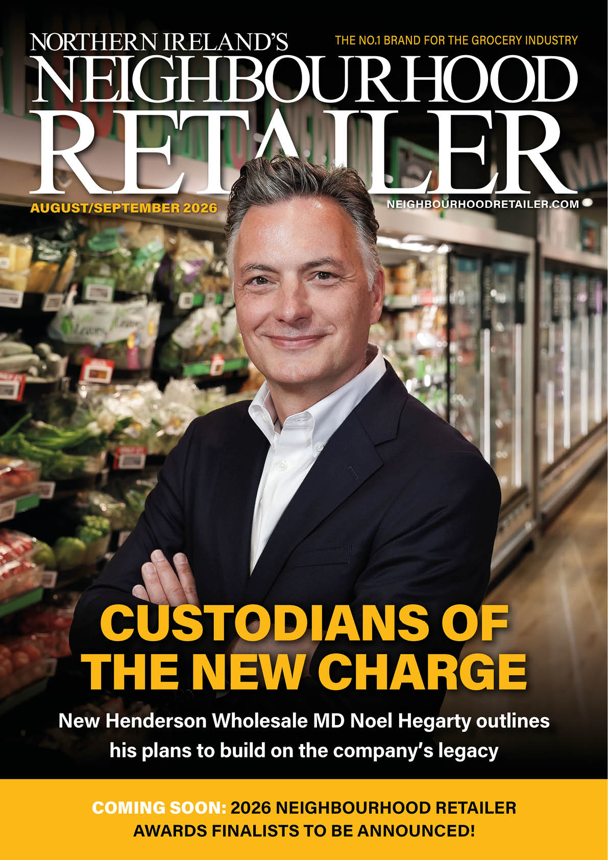 A person in a dark suit and white shirt stands confidently with arms crossed in a grocery store aisle filled with fresh produce and refrigerated items, featured on the cover of Northern Ireland's Neighbourhood Retailer magazine. Description generated by AI