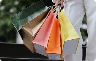 A stylish Asian woman walks happily through a modern city shopping mall. She’s holding luxury bags, enjoying the bustling urban atmosphere, surrounded by fashionable stores and other cheerful shoppers
