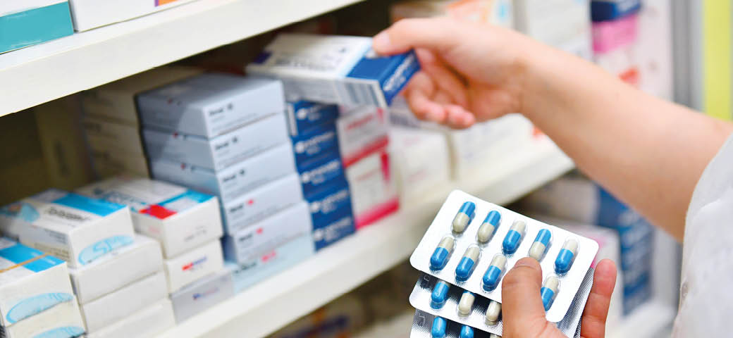 Pharmacist holding medicine box and capsule pack in pharmacy drugstore.
