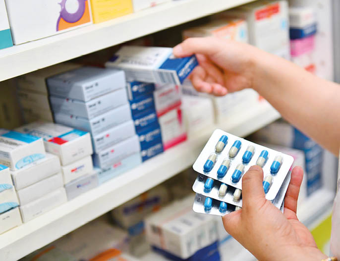 Pharmacist holding medicine box and capsule pack in pharmacy drugstore.
