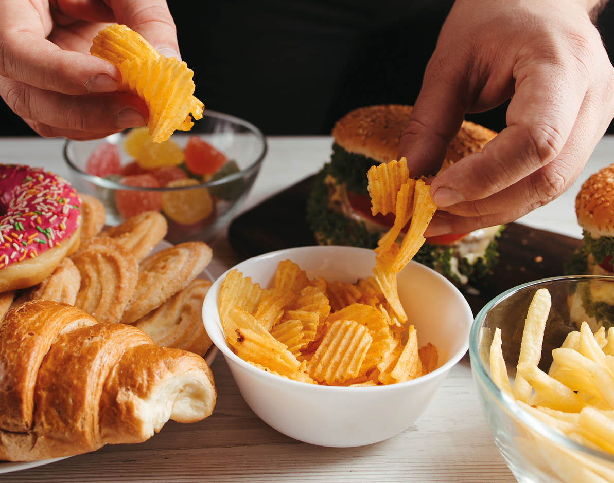 Unhealthy snack, junk food, compulsive overeating. Man overeating unhealthy meals taking hamburger and potato chips from plate