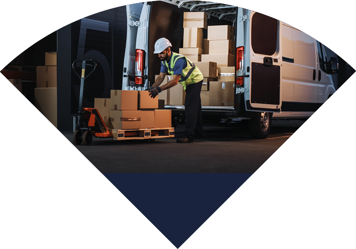 Outside of Logistics Distributions Warehouse Delivery Van: Worker Unloading Cardboard Boxes on Hand Truck, Online Orders, Purchases, E-Commerce Goods, Food, Medical Supply. Evening Shot