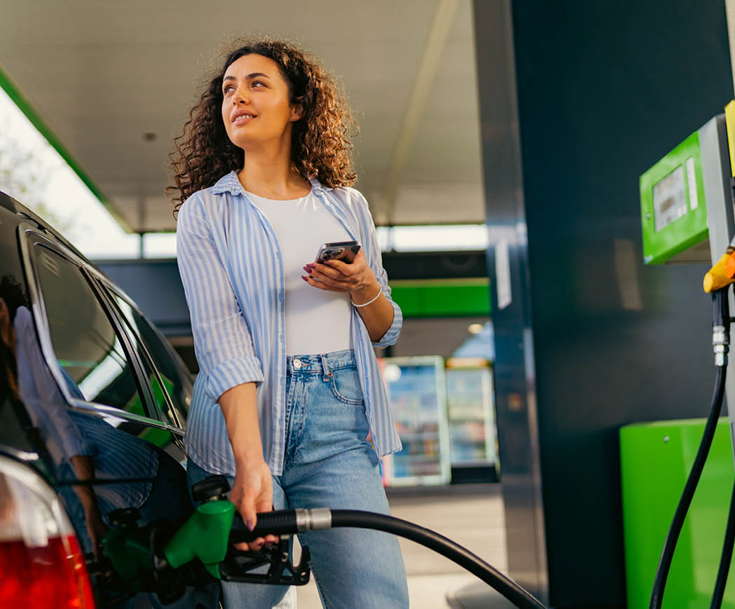 A young beautiful woman does not follow the safety rules and uses the phone while filling her car gas tank