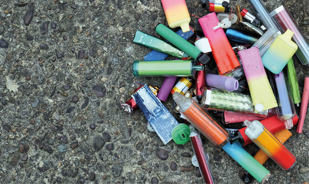 A collection of discarded electronic cigarette vapes have been collected and placed together over a worn concrete floor