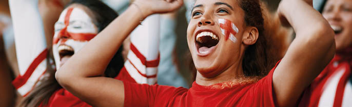 Female soccer fans of England watching and celebrating their team's victory. English female spectators enjoying after a win at stadium.