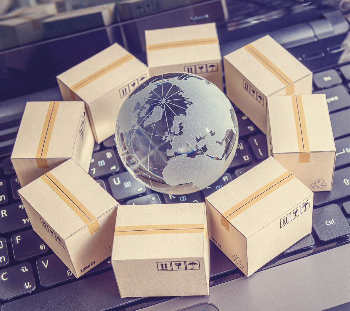 A small globe is surrounded by eight miniature cardboard boxes arranged in a circle on a laptop keyboard. Description generated by AI