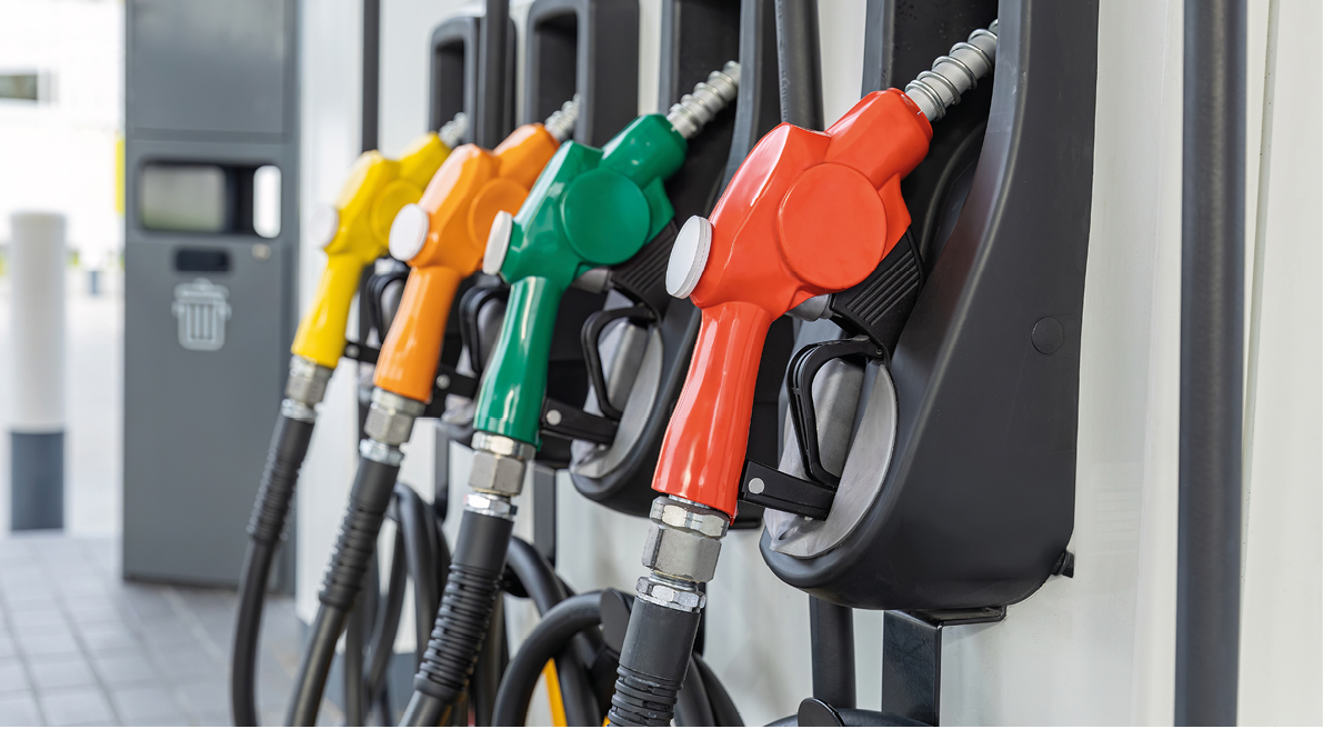 Four fuel pump nozzles in yellow, orange, green, and red are lined up at a gas station. Description generated by AI