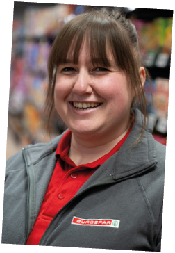 A person wearing a red polo shirt and a gray jacket with a Eurospar logo is smiling in a store aisle. Description generated by AI