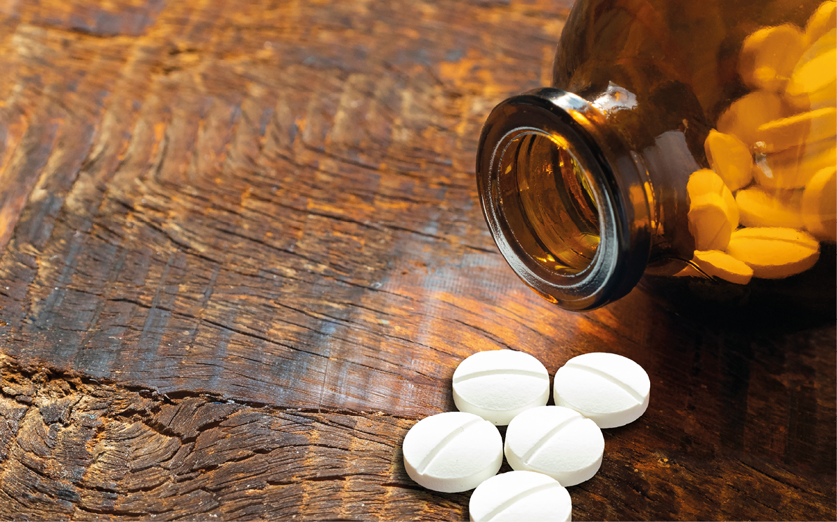 A brown glass bottle is tipped over on a wooden surface with several white round pills spilled out in front of it. Description generated by AI