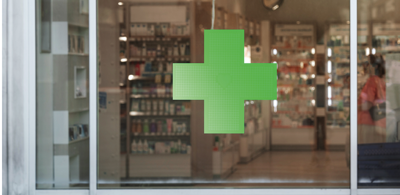 Green cross sign with neon light mounted on pharmacy shop window case outdoor