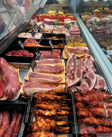 A meat display case in a butcher shop or market shows various cuts of raw and marinated meats arranged in trays and on wooden boards. Description generated by AI