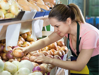 A person wearing a pink shirt and green apron is selecting onions from a display in a grocery store. Description generated by AI