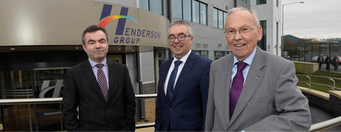 Three adults in business attire stand outside a building with a sign that reads “Henderson Group" while smiling at the camera. Description generated by AI