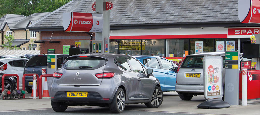 Several cars are parked and waiting at a Texaco gas station with a convenience store in the background. Description generated by AI