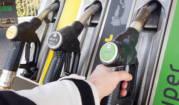 A person is holding a green fuel pump nozzle labeled “super" at a gas station with other fuel nozzles visible nearby. Description generated by AI