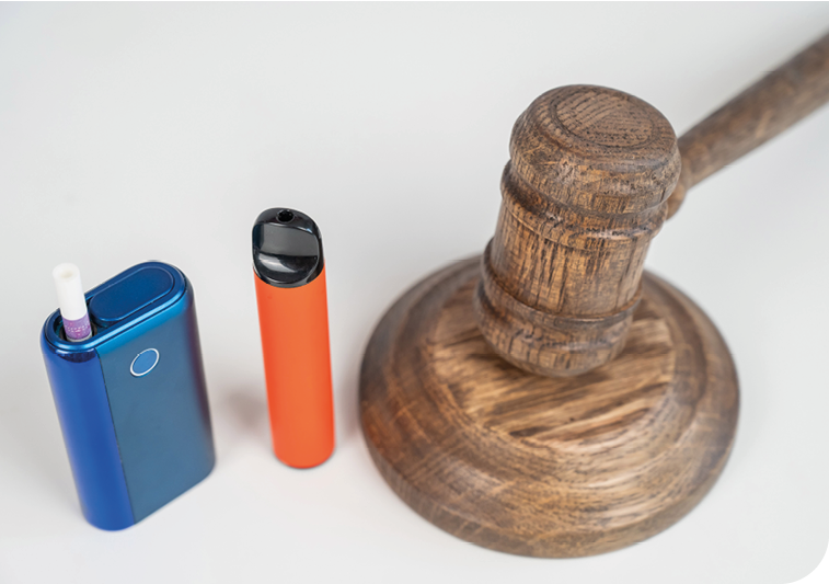 A wooden judge's gavel rests next to two electronic vaping devices on a white surface. Description generated by AI