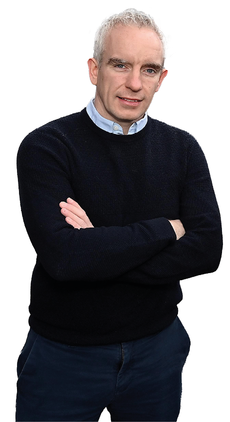 A person with short gray hair wearing a black sweater over a light blue collared shirt stands with arms crossed and a slight smile. Description generated by AI
