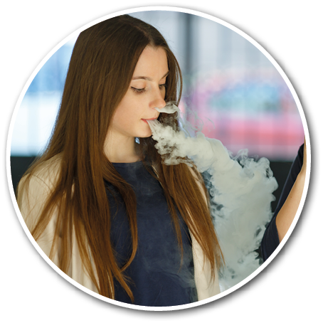 Two adults with long hair are using vape devices indoors, with one exhaling a large cloud of vapor. Description generated by AI