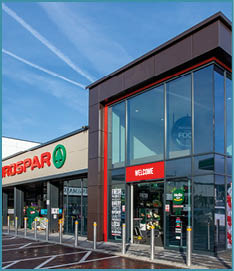 A modern Eurospar supermarket entrance decorated with a red and white balloon arch and a wet parking lot with marked spaces including a handicap spot. Description generated by AI
