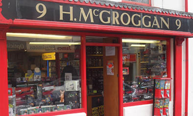 A storefront with a red frame displays various model cars and collectibles inside a shop named T.M. Groggan. Description generated by AI