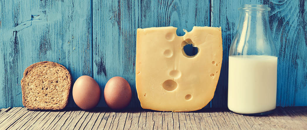 a toast, some eggs, a piece of Swiss cheese and a bottle with milk on a rustic wooden table, against a blue rustic wooden background, with a filter effect