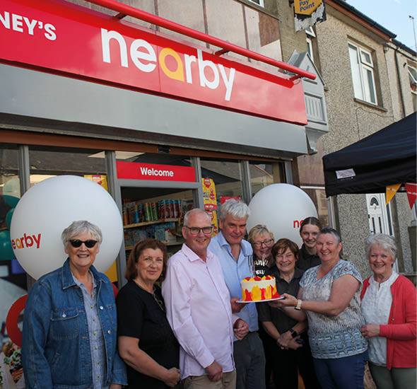 A group of people are standing in front of a store, posing for a picture. One of the women is holding a cake. AI generated content