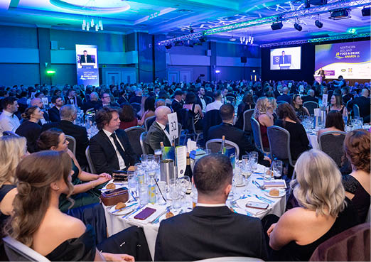 A large group of people are sitting at tables in a banquet hall. They are dressed in formal attire, with many of them wearing ties. The tables are set with wine glasses, cups, and other dining utensils. The attendees are engaged in conversation and enjoying their time at the event. AI generated content