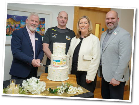 Four people are standing around a cake, with one of them holding a knife. The cake is decorated with white flowers. AI generated content
