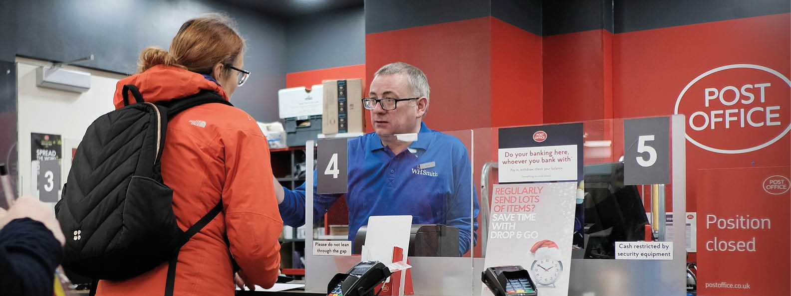 A woman in a red coat is standing at a counter, talking to a man behind the counter. AI generated content