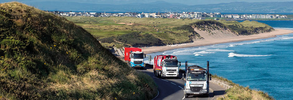 A truck is driving on a road near the ocean, with another truck following behind it. The road is curvy and overlooks the ocean, providing a scenic view for the drivers. AI generated content
