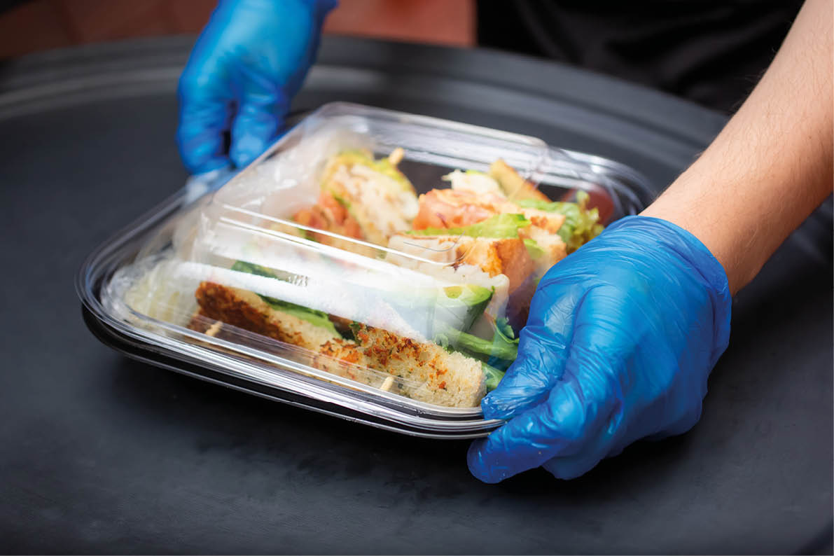 A view of an employee preparing to pack a food to-go containers, in a restaurant kitchen setting.