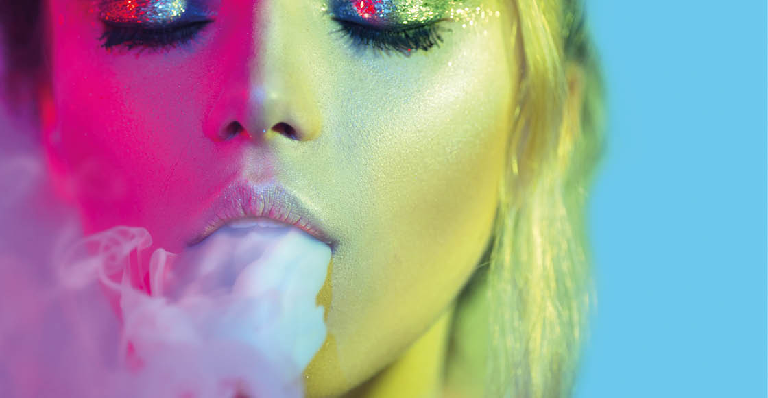 Fashion art portrait of beauty model woman in bright lights with colorful smoke. Smoking girl, Close up of a female inhaling from an electronic cigarette. Night life concept