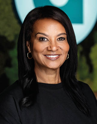 A woman is smiling in front of a green sign. Description generated by AI