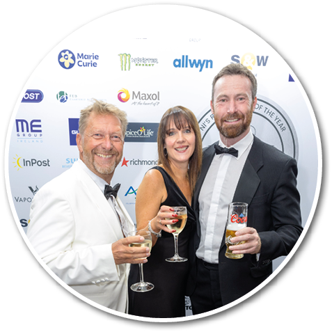 Three people standing in front of a wall, two men and a woman, holding wine glasses. Description generated by AI