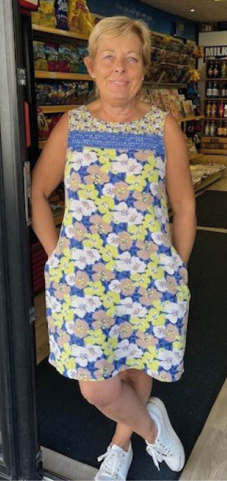 A woman in a blue and yellow dress is standing in front of a store. Description generated by AI