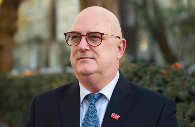 A bald man wearing glasses and a suit. Description generated by AI