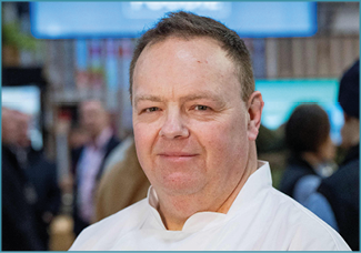 A man wearing a white shirt with the word Foodie on it. Description generated by AI
