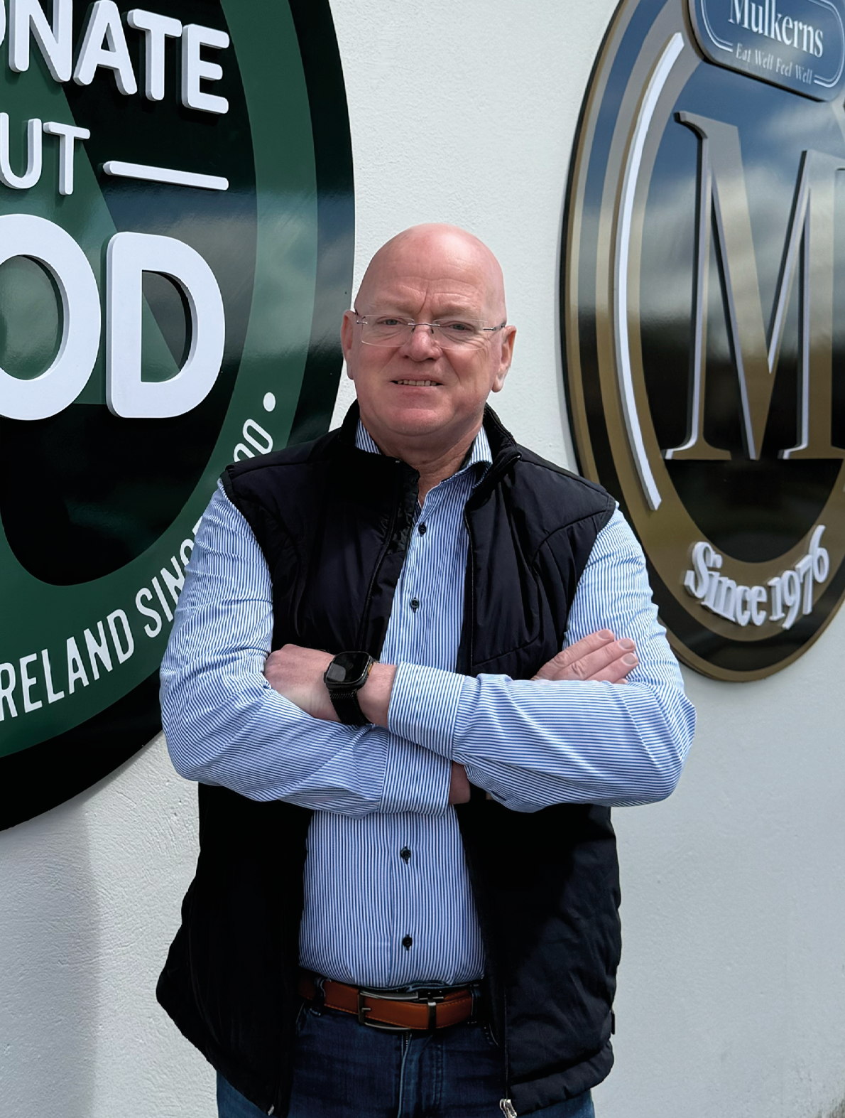 A man standing in front of a green sign that says “Eat Passionate About Food". Description generated by AI