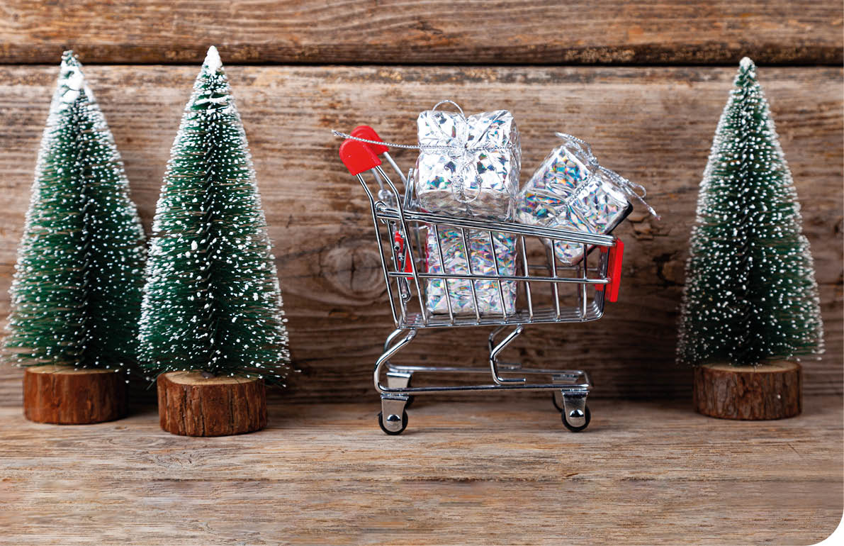 Shopping cart with gifts and Christmas trees on a wooden background. Holiday sale.