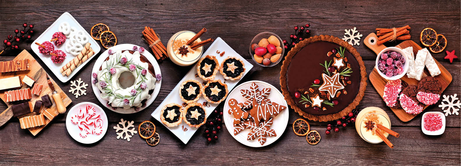 Assorted Christmas holiday desserts and sweets. Top view panoramic table scene over a rustic wood background. Bundt cake, chocolate pie, mincemeat tarts, cookies, fudge and eggnog.