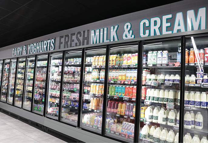 A supermarket aisle with glass-door refrigerators stocked with various dairy products including milk, yoghurts, and cream. Description generated by AI