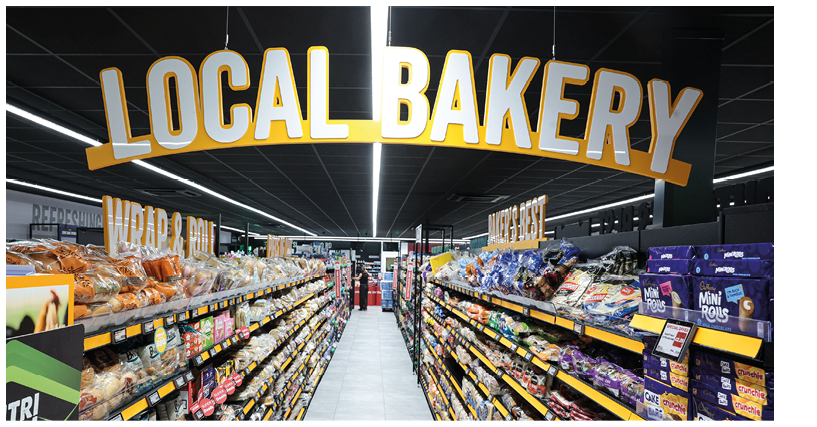 A brightly lit aisle in a grocery store labeled “Local Bakery" with shelves stocked with various bread, rolls, and baked goods on both sides. Description generated by AI